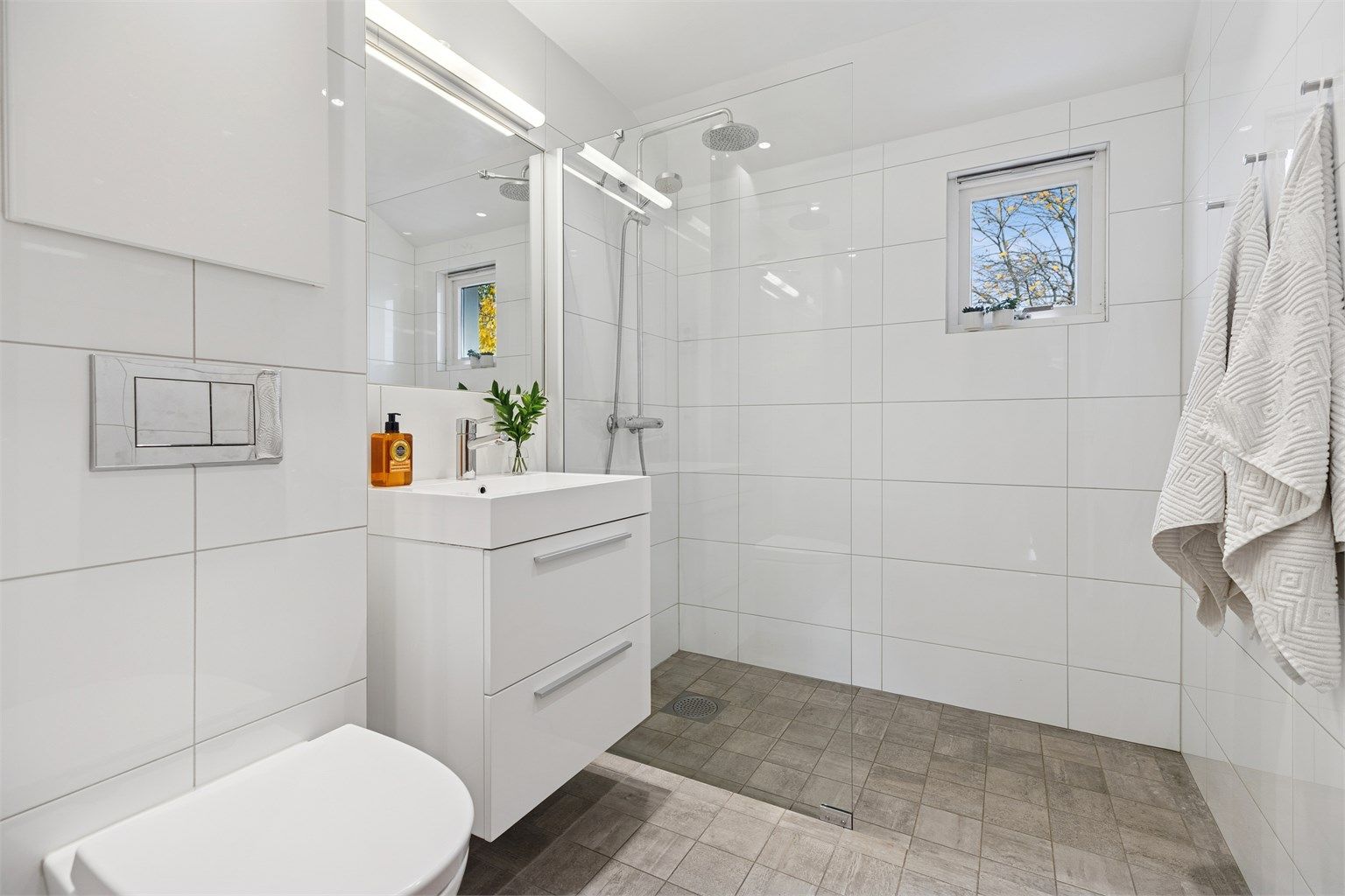 Klassisk, pent og flislagt baderom med gulvarme og et romslig dusjhjørne.