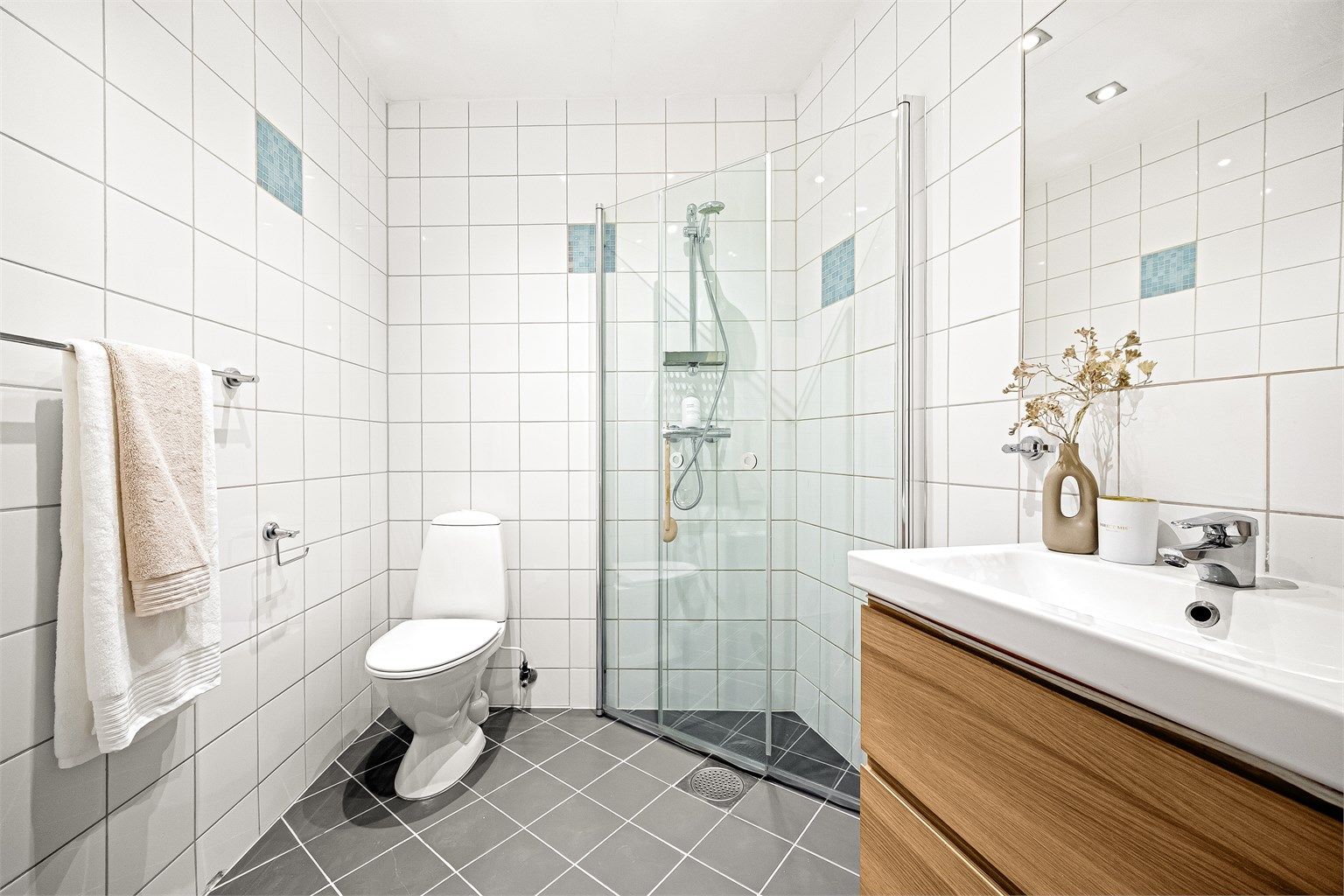 Badet har et tidløst uttrykk med hvite fliser på veggene, mørke gulvfliser og innslag av blå mosaikkfliser.