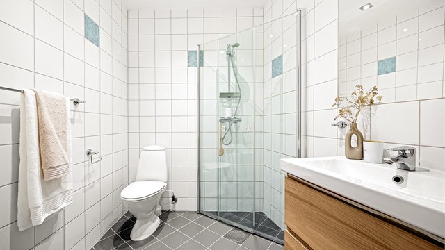 Badet har et tidløst uttrykk med hvite fliser på veggene, mørke gulvfliser og innslag av blå mosaikkfliser.