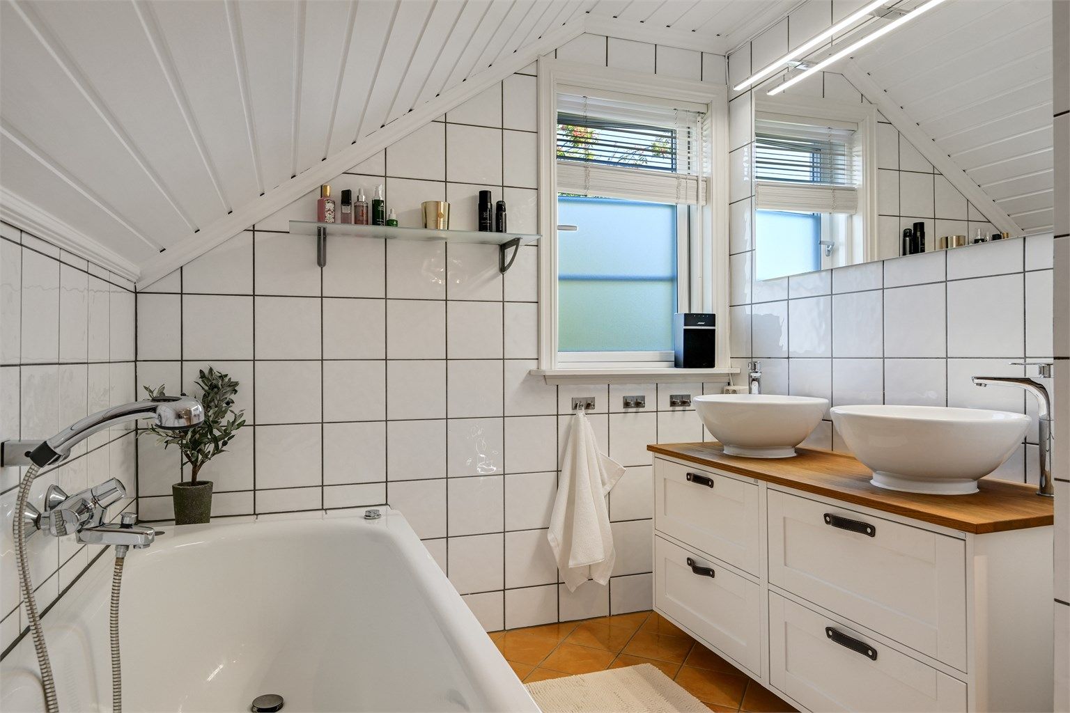 Innfliset badekar plassert under skråtaket med vindu som gir godt dagslys.