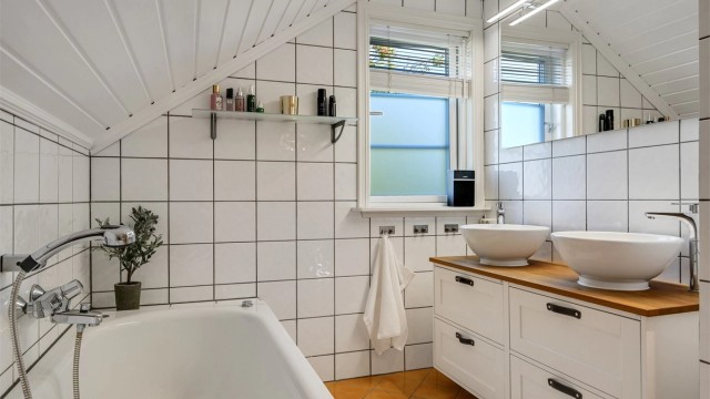 Innfliset badekar plassert under skråtaket med vindu som gir godt dagslys.