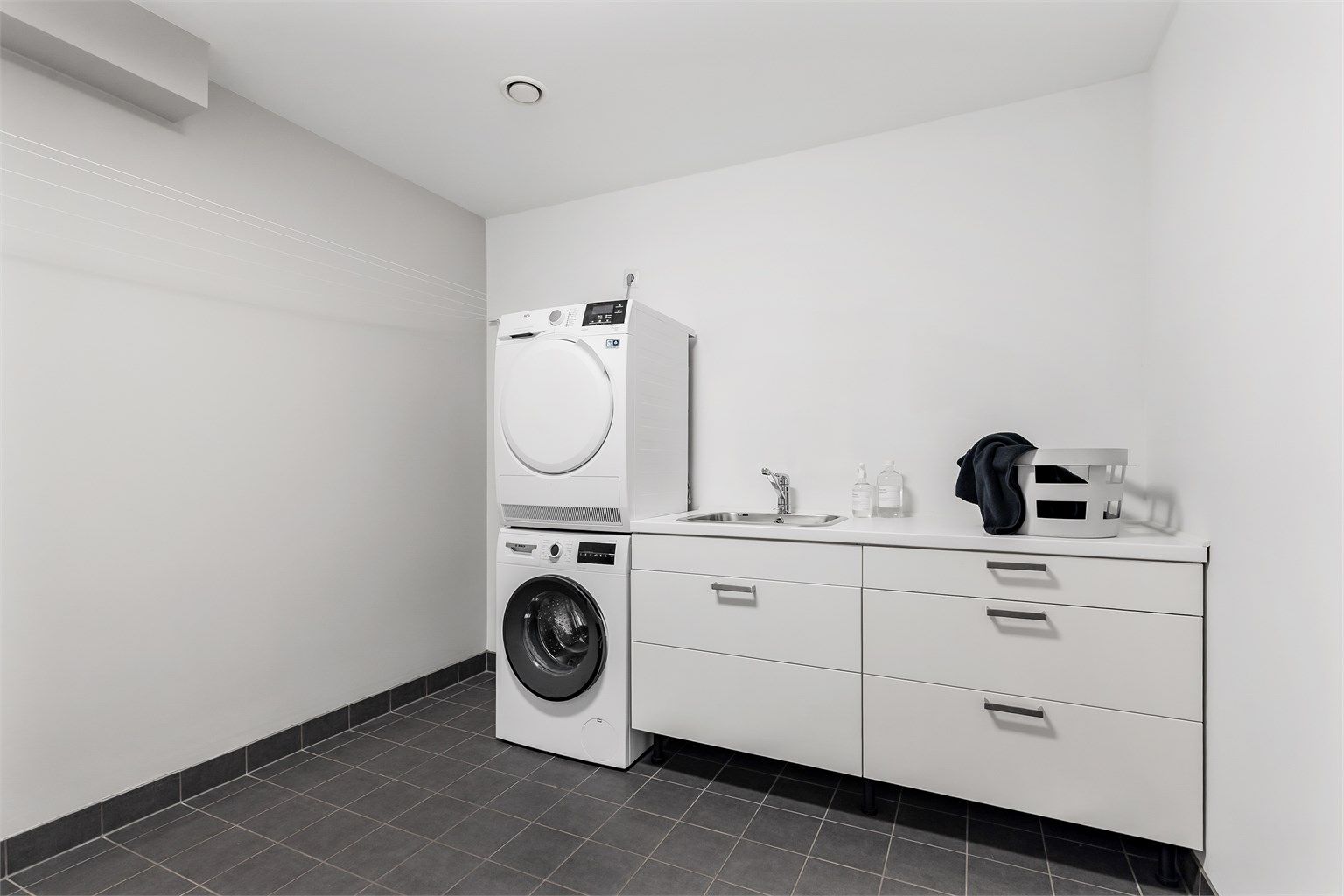 Vaskerom med flislagt gulv med varme og vegger i malte flater. Baderomsinnredning med slette fronter. Benkeplate av laminat. Nedfelt oppvaskkum av rustfritt stål med ett-greps. Mekanisk avtrekksventil på vegg. Opplegg for vaskemaskin/tørketrommel.