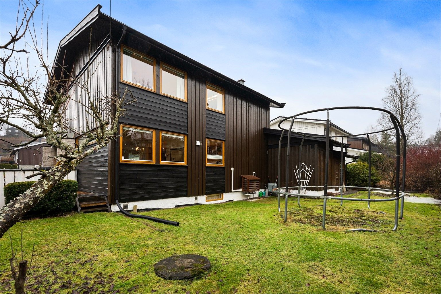 Enebolig fra 1974 over tre plan, beliggende på en tilnærmet flat tomt med plen og beplantning.