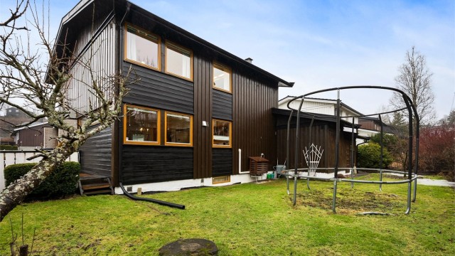 Enebolig fra 1974 over tre plan, beliggende på en tilnærmet flat tomt med plen og beplantning.