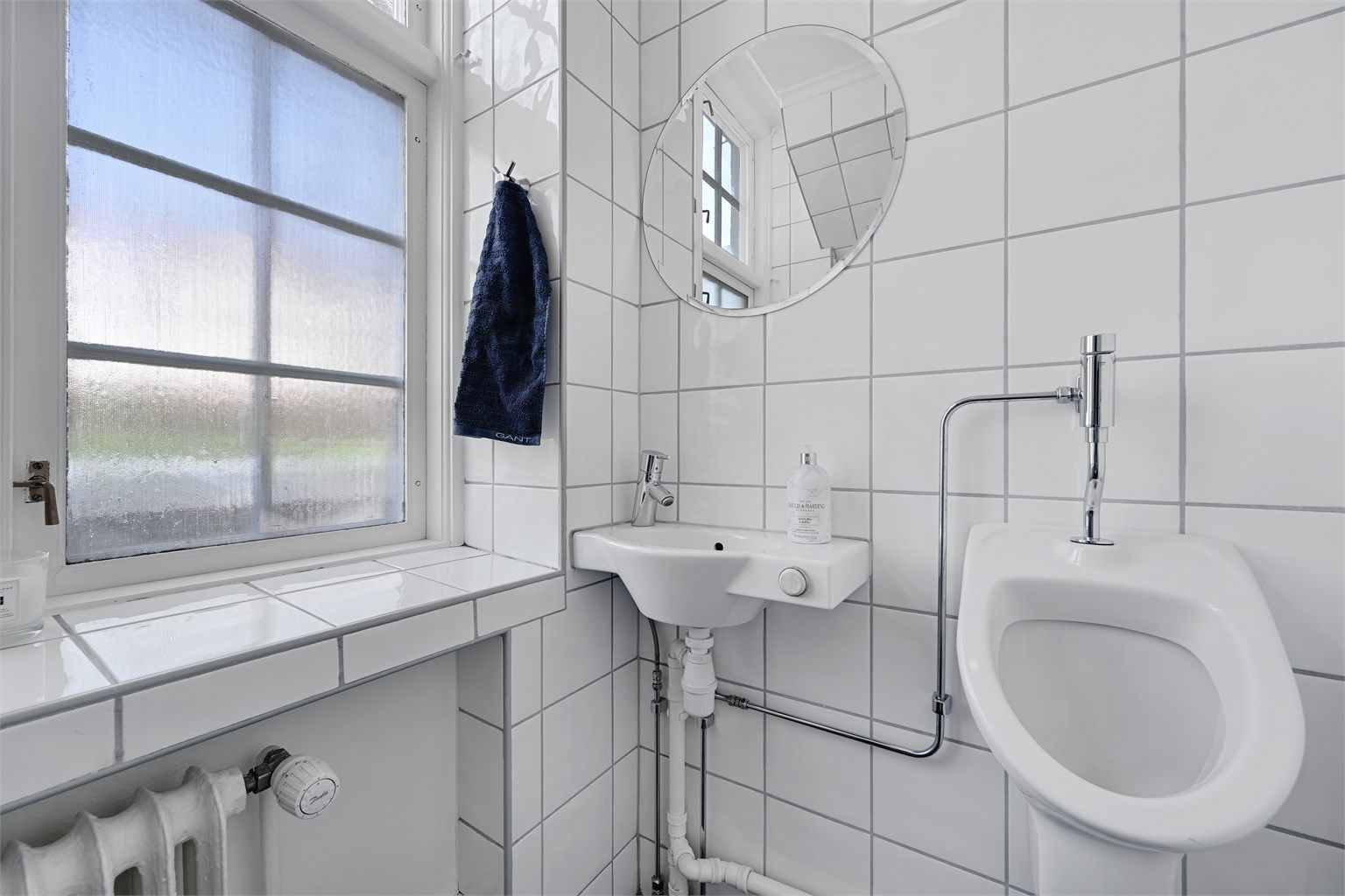 Praktisk toalettrom i første etasje med flislagte vegger, håndvask og urinal.