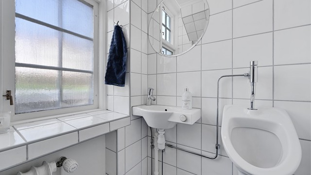Praktisk toalettrom i første etasje med flislagte vegger, håndvask og urinal.