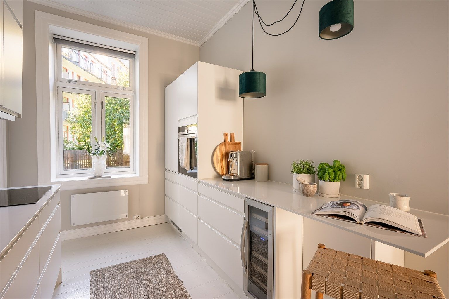 Kjøkkeninnredning fra Designia med hvite, glatte fronter, benkeplate av komposittstein og nedfelt kjøkkenvask med armatur