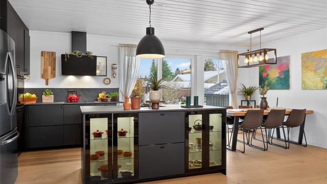 Stor kjøkkenøy med rikelig oppbevaringsplass og nedfelt oppvaskkum. Fine glasshyller med belysning vendt mot stuen
