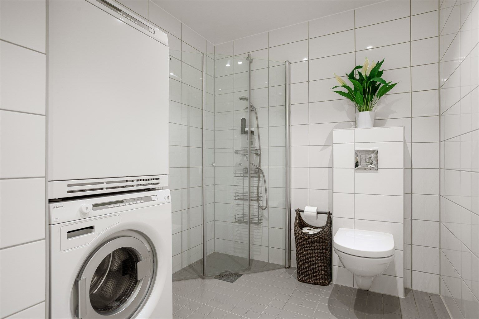 Dusjbad/wc - Innfelte downlights i himling, vegghengt toalett med utenpåliggende sisterne og rettvinklete dusjvegger i herdet glass. Opplegg for vaskemaskin og kondenstørketrommel. 