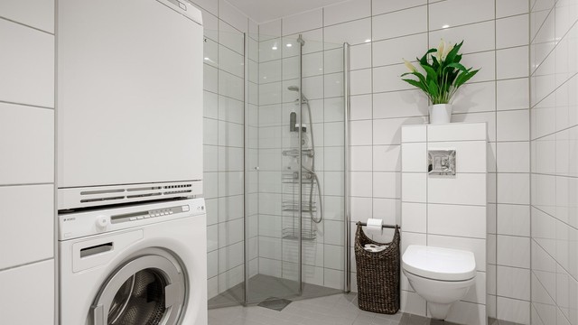 Dusjbad/wc - Innfelte downlights i himling, vegghengt toalett med utenpåliggende sisterne og rettvinklete dusjvegger i herdet glass. Opplegg for vaskemaskin og kondenstørketrommel.