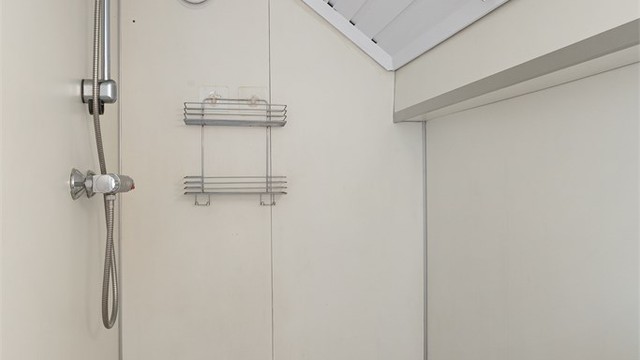 Dusjsonen er plassert under skråtaket, med veggmontert dusjbatteri og sluk i gulvet.