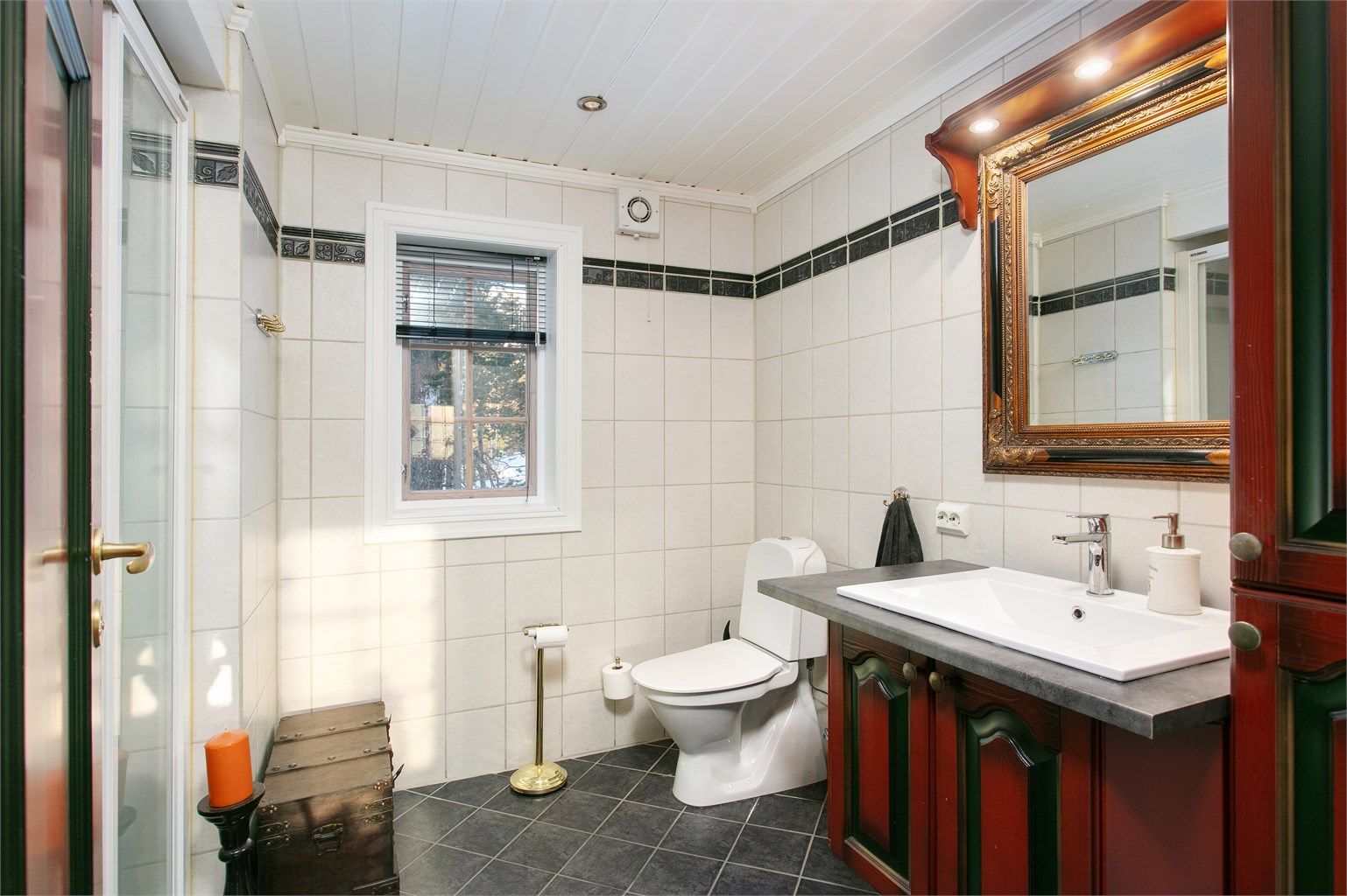 Romslig bad med flislagt gulv med gulvvame, flislagte vegger, baderomsinnredning, wc og dusjhjørne