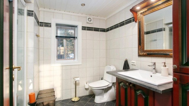 Romslig bad med flislagt gulv med gulvvame, flislagte vegger, baderomsinnredning, wc og dusjhjørne