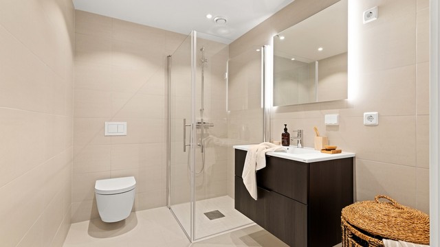 Badet har en ren og moderne utforming med store, sandfargede fliser og vannbåren gulvvarme.