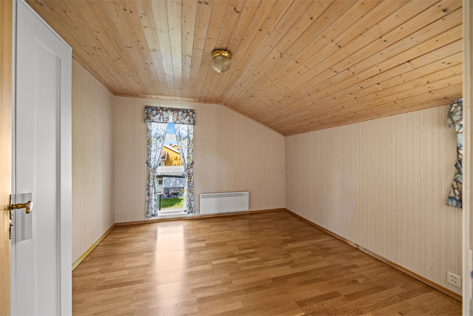 Soverom i første etasje med trepanel i himling og vindu mot nabolaget.