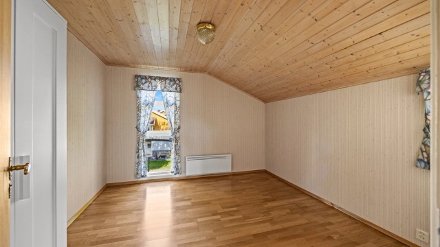 Soverom i første etasje med trepanel i himling og vindu mot nabolaget.