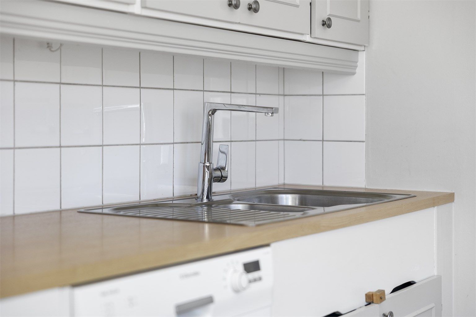 Kjøkkenet er utstyrt med oppvaskmaskin og har fliser mellom benkeplate i laminat og overskap.