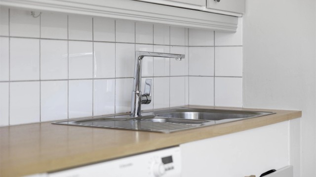 Kjøkkenet er utstyrt med oppvaskmaskin og har fliser mellom benkeplate i laminat og overskap.