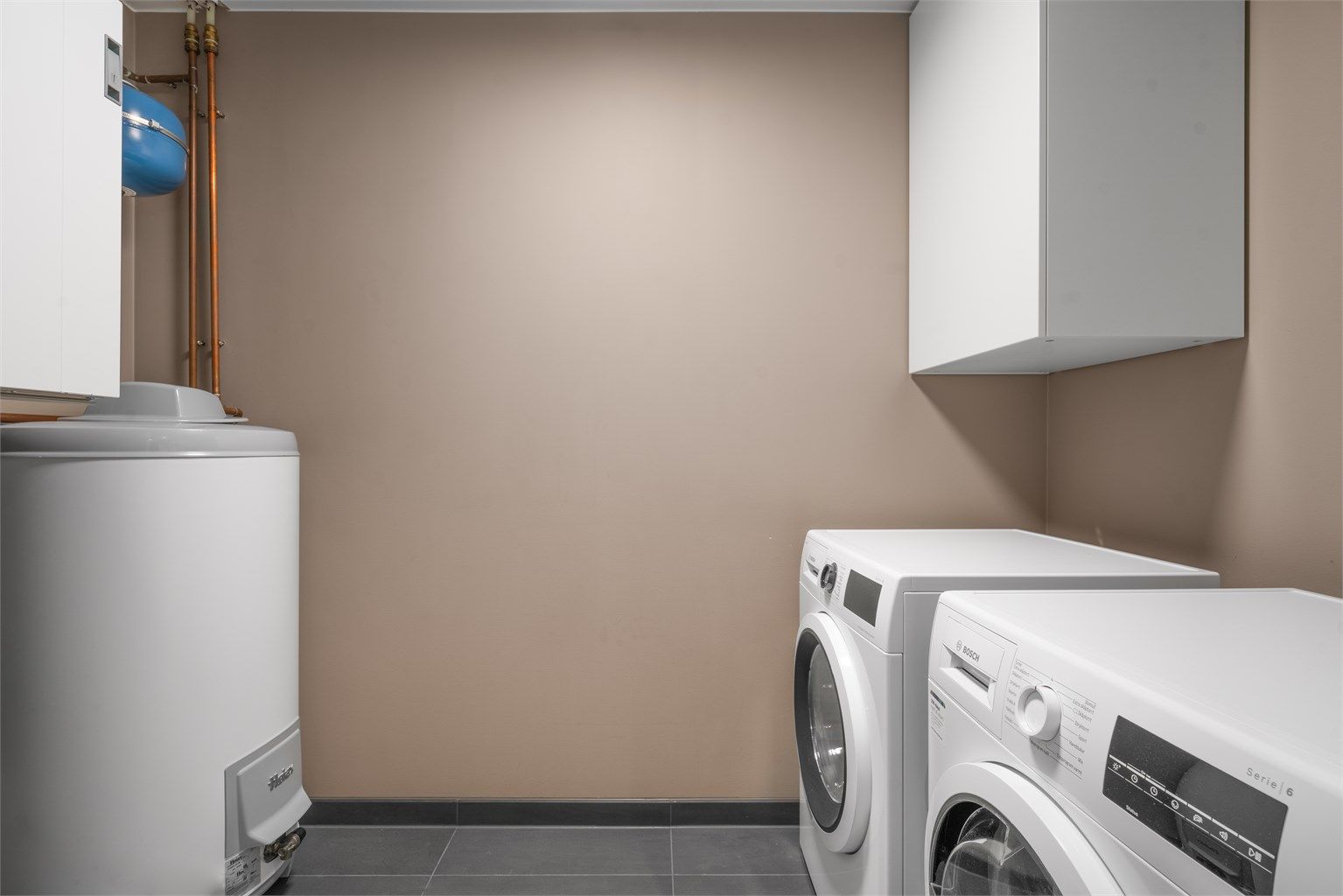 Eget vaskerom med flislagt gulv, varmtvannsbereder og opplegg for vaskesøyle.