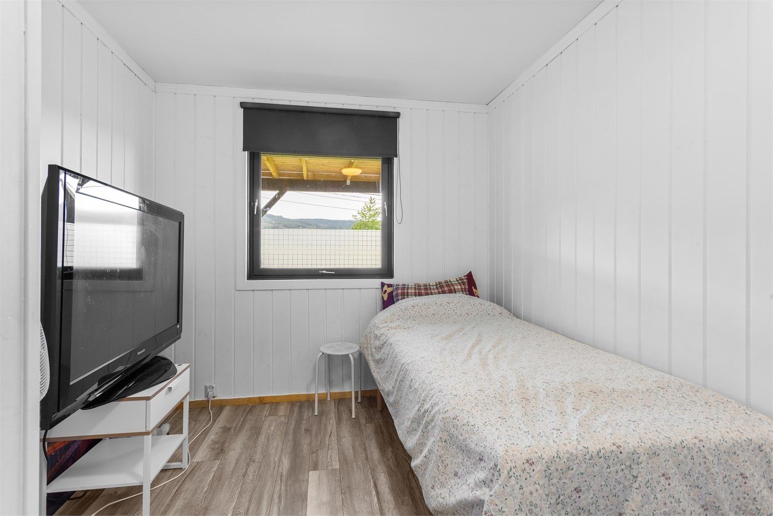 Soverom i underetasjen med hvitmalt trepanel på veggene og plass til seng.