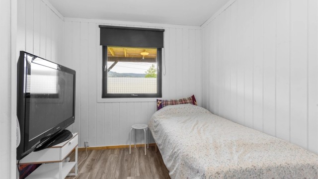 Soverom i underetasjen med hvitmalt trepanel på veggene og plass til seng.