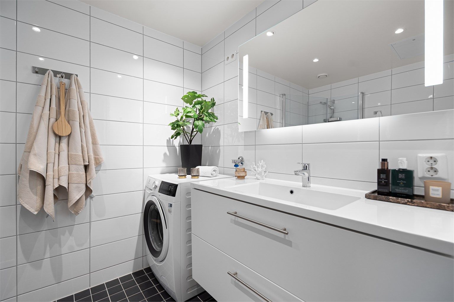 Stilrent baderom fra 2019 med opplegg for vaskemaskin, flislagt gulv med gulvvarme, flislagte vegger samt malt himling med downlights. Badet er utstyrt med vegghengt servantinnredning, speil med sidelys, vegghengt toalett.