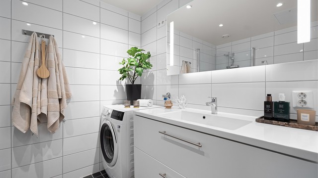 Stilrent baderom fra 2019 med opplegg for vaskemaskin, flislagt gulv med gulvvarme, flislagte vegger samt malt himling med downlights. Badet er utstyrt med vegghengt servantinnredning, speil med sidelys, vegghengt toalett.