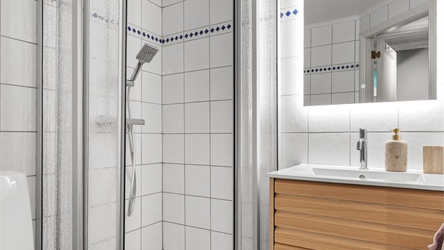 Bad med flislagt gulv med gulvvarme. Vegghengt servantinnredning. Ovenpåliggende servant med armatur. Speil med sidelys. Dusjnisje med vegg og skyvedører av plast og metall. Vegghengt dusjarmatur (hånddusj og regndusj). Gulvstående toalett.