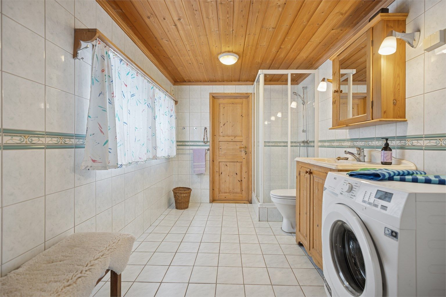 Flislagt bad med gulvvarme, dusjhjørne, servant, gulvstående toalett og opplegg for vaskemaskin