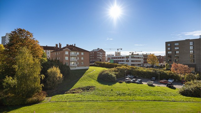 Utsikt over borettslagets store, parkmessige fellesområde, som rammer inn hverdagen med grønne plener og frodige trær. Her bor du midt i byen, men med naturen rett utenfor vinduet.