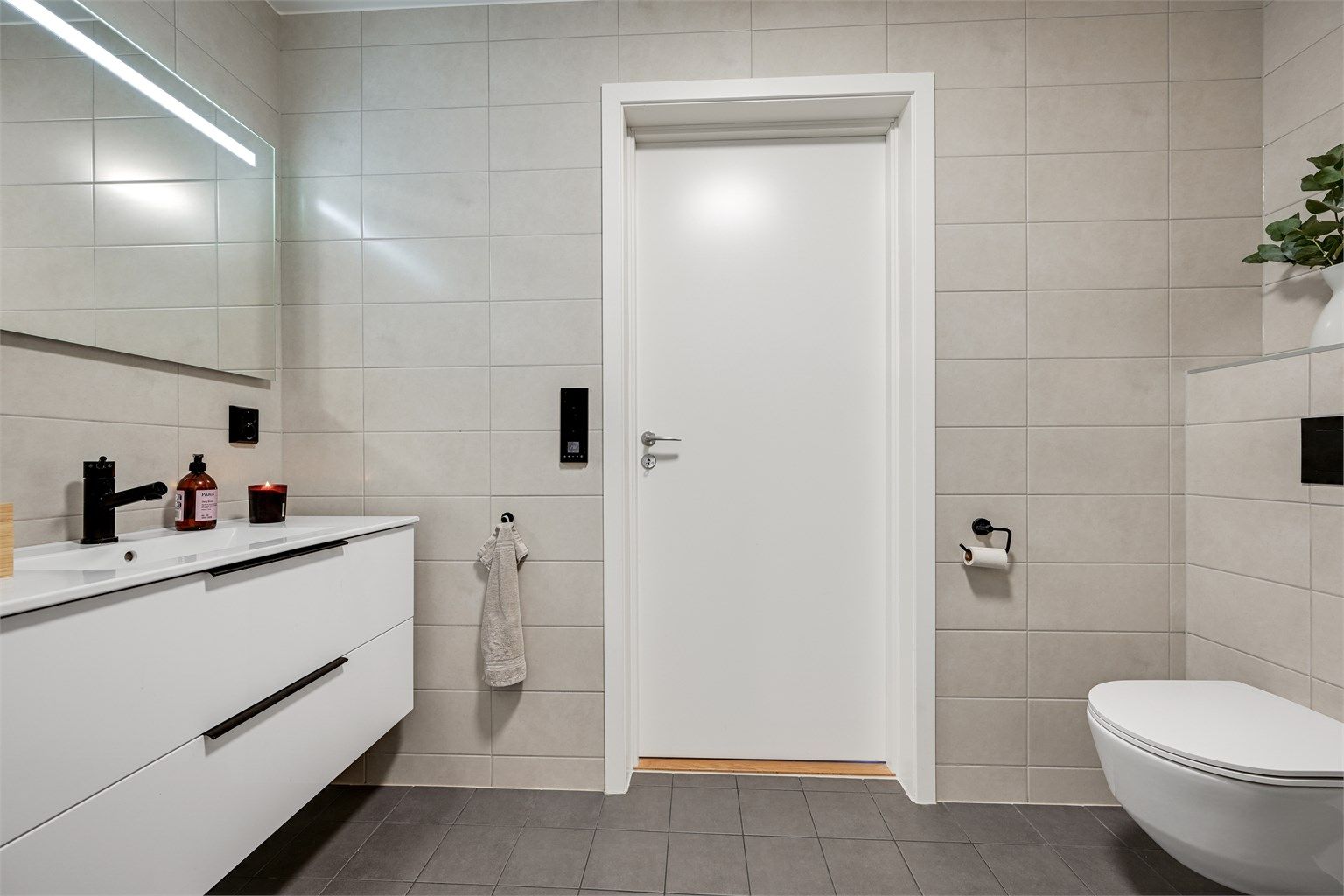Badet fremstår moderne og innbydende med flislagte gulv og vegger, gulvvarme, vegghengt toalett og dusjnisje med glassdør.