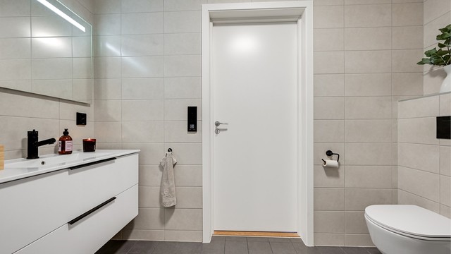 Badet fremstår moderne og innbydende med flislagte gulv og vegger, gulvvarme, vegghengt toalett og dusjnisje med glassdør.