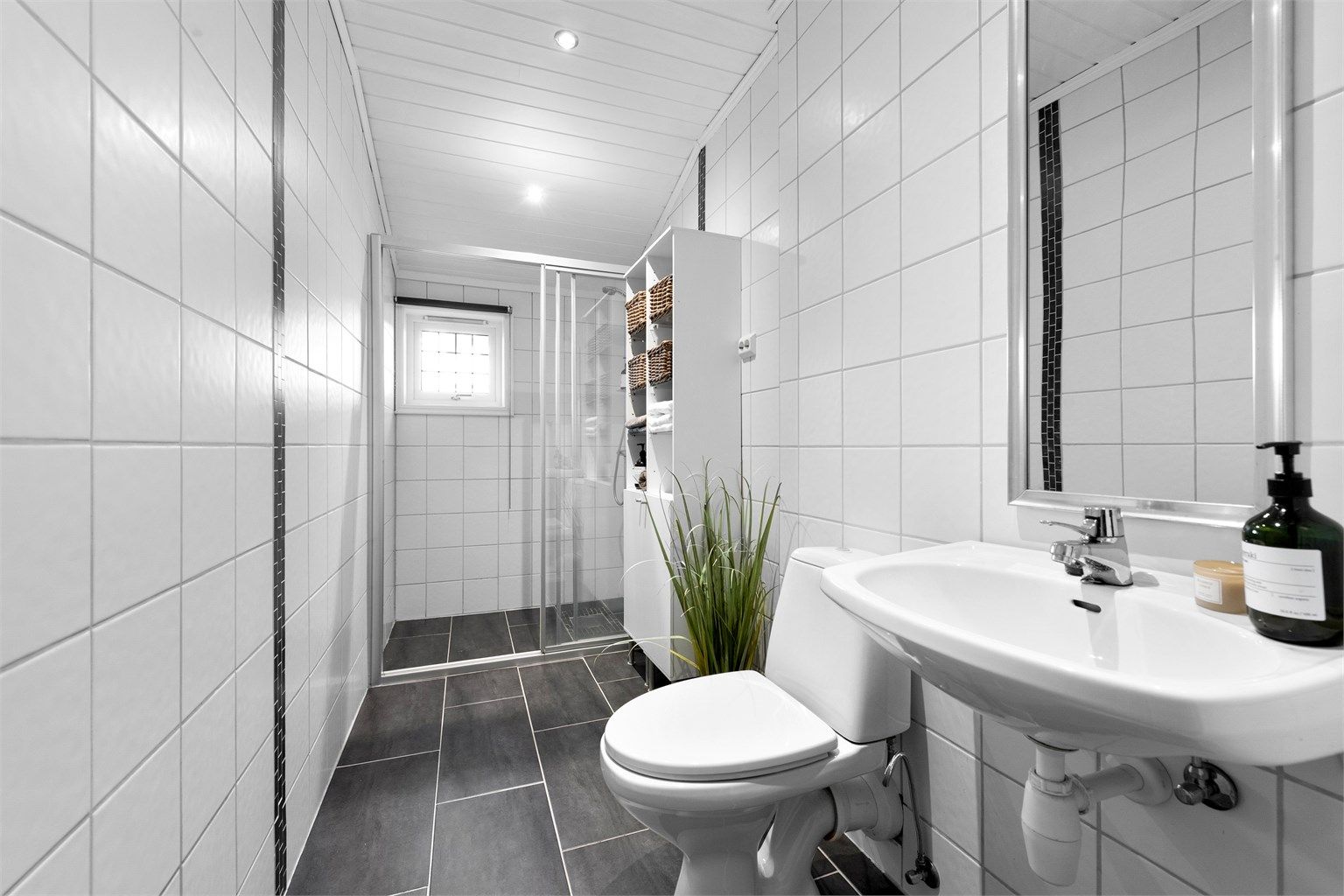 Bad i første etasje med flislagt gulv og vegger, oppgradert ca. 2005. Rommet har gulvvarme og dusjnisje med skyvedører og vegghengt armatur