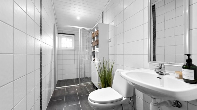 Bad i første etasje med flislagt gulv og vegger, oppgradert ca. 2005. Rommet har gulvvarme og dusjnisje med skyvedører og vegghengt armatur