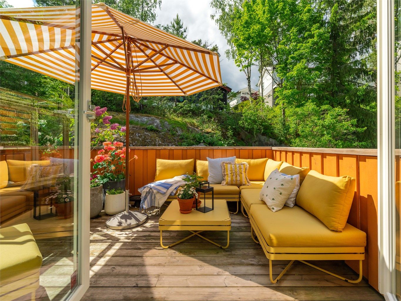 Verandaen er designet slik at man kan sitte lunt og godt i solen fra tidlig om våren til langt utpå høsten, og hele området bak huset føles skjermet, som en rolig oase for seg selv. 