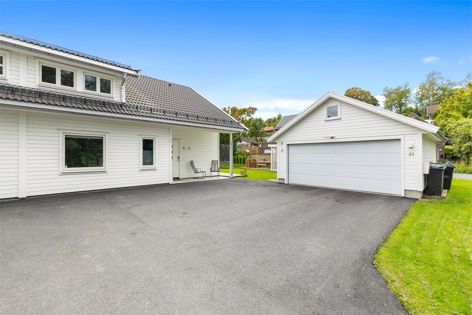 Asfaltert gårdsplass og frittstående garasje med lader for elbil.