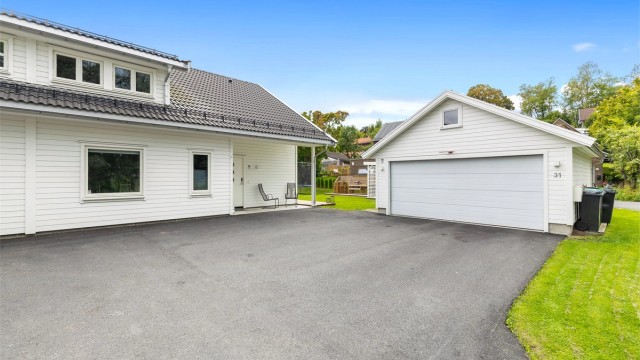 Asfaltert gårdsplass og frittstående garasje med lader for elbil.