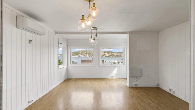 Stuen er lys og romslig, med vinduer som rammer inn utsikten mot sjøen.