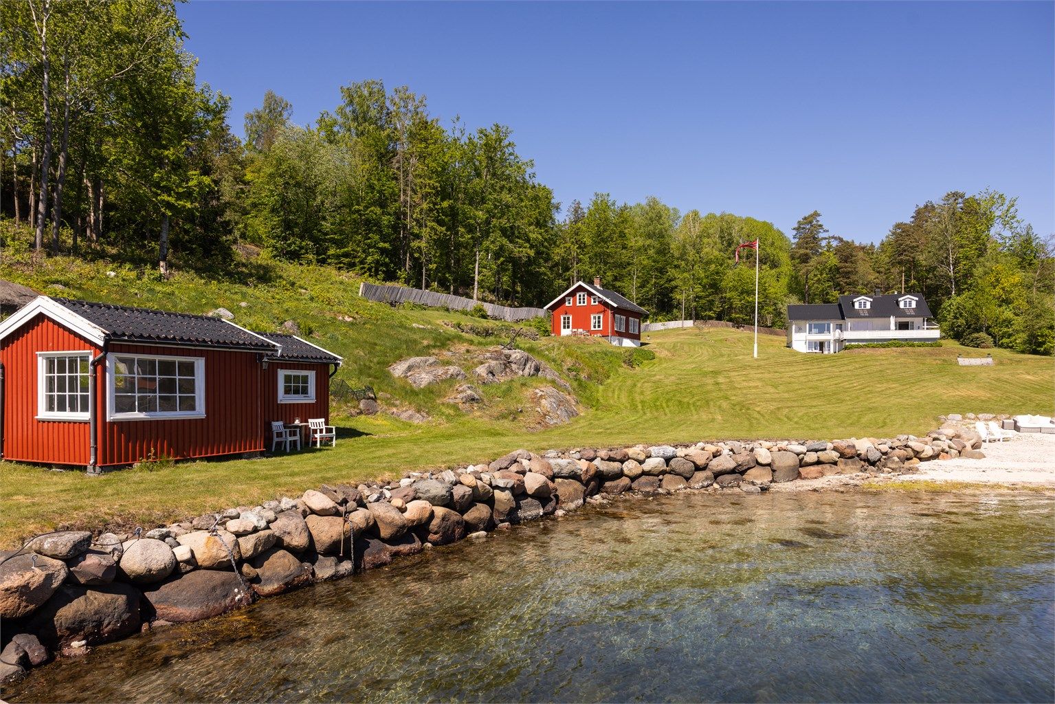 En praktfull, inngjerdet strandtomt bestående av en stor, parkmessig opparbeidet gressplen, egen lang sandstrand samt en elegant strandpromenade i stein