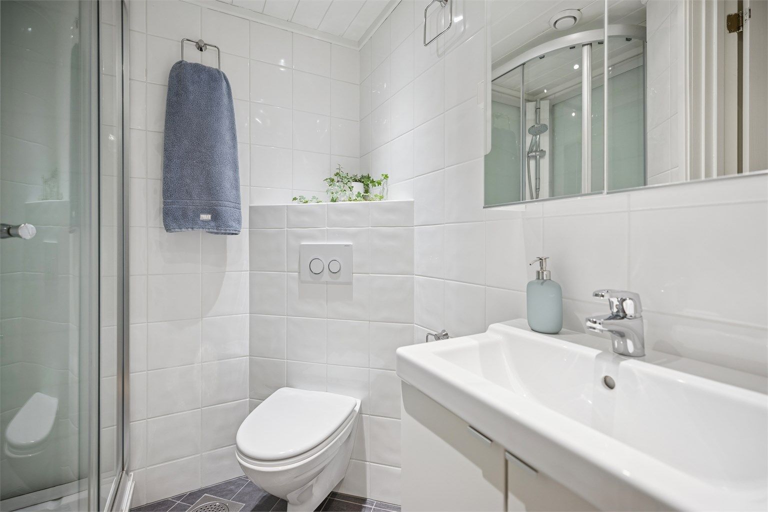 Pent flislagt bad med gulvvarme, vegghengt servantinnredning, dusjkabinett og vegghengt toalett.