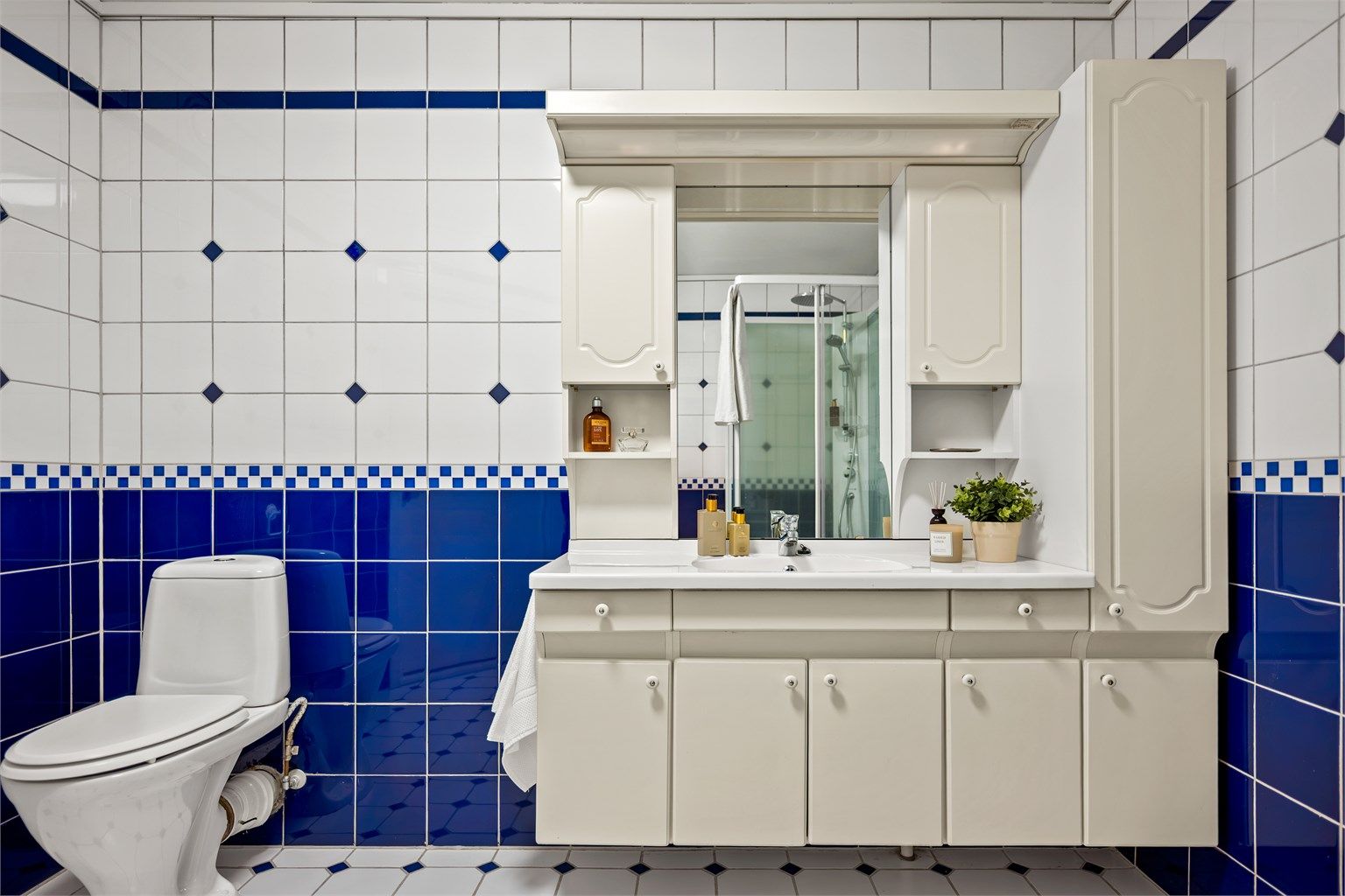 Badet er helfliset og utstyrt med dusjkabinett, toalett og en romslig servantinnredning med speil samt overlys.
