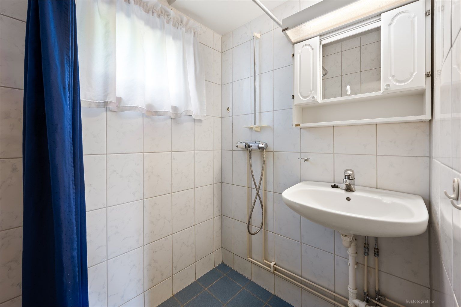 Badet har vegghengt servant og dusj i hjørne med veggmontert dusjarmatur samt opplegg for dusjforheng. Det er også gulvvarme.