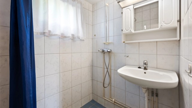 Badet har vegghengt servant og dusj i hjørne med veggmontert dusjarmatur samt opplegg for dusjforheng. Det er også gulvvarme.