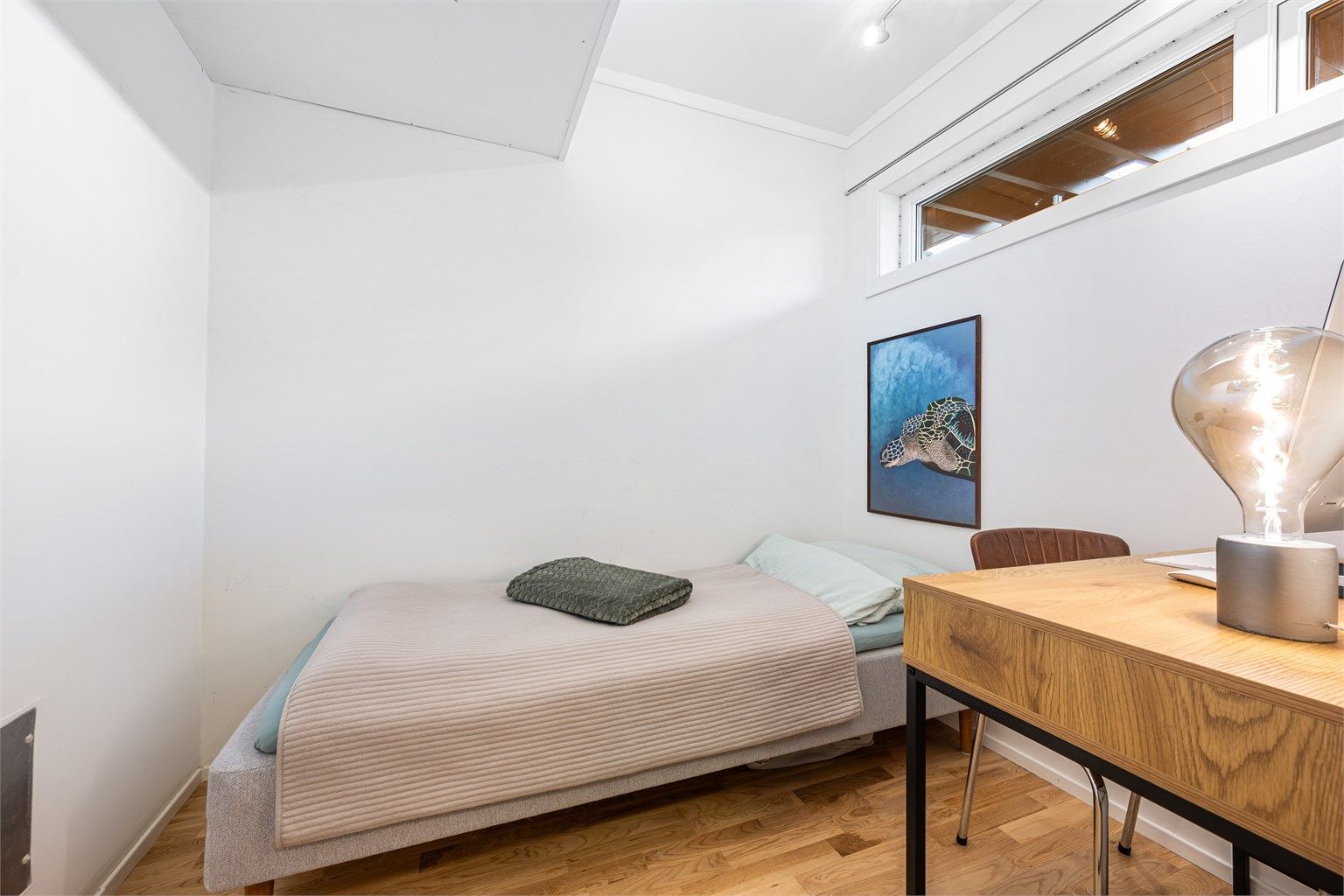 Innvendig bod har plass til både seng og kontor. Parkett på gulv og lyse veggflater og tak. Det er lite vindu som kan åpnes. 
