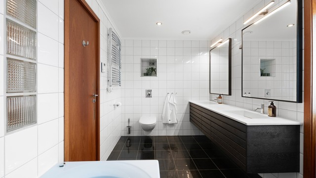 Badet mot syd har dobbel servant med mørk baderomsinnredning, speil med overlys og gulvvarme.