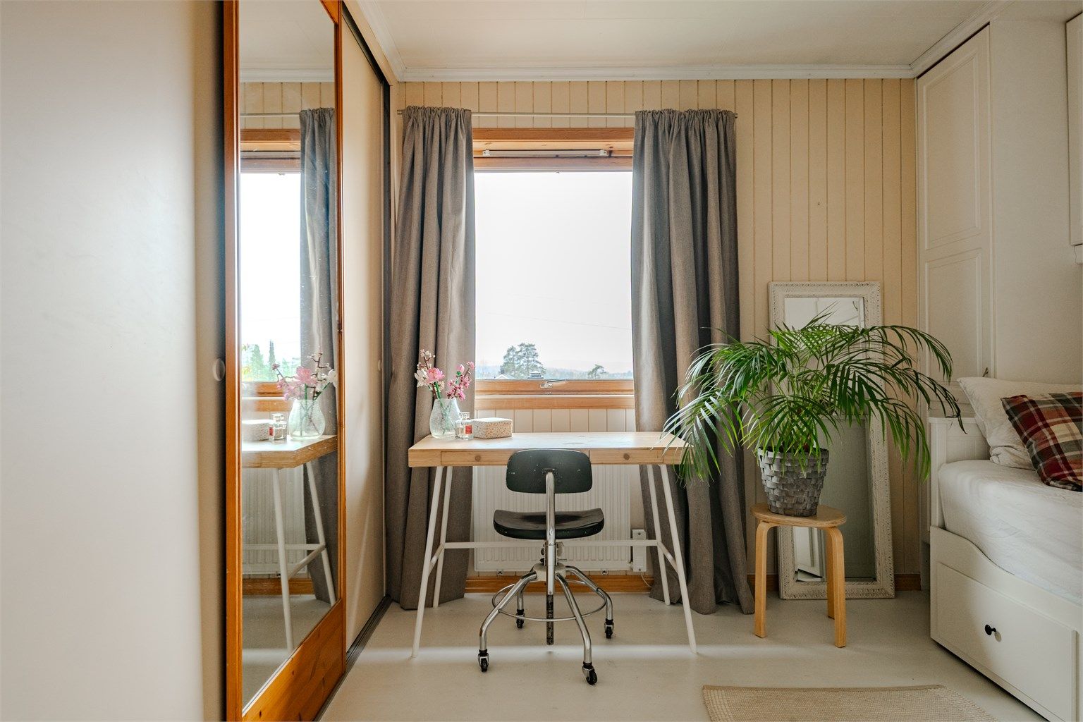 Romslig skyvedørsgarderobe med speildør og vindu som vender ut mot grønne omgivelser.