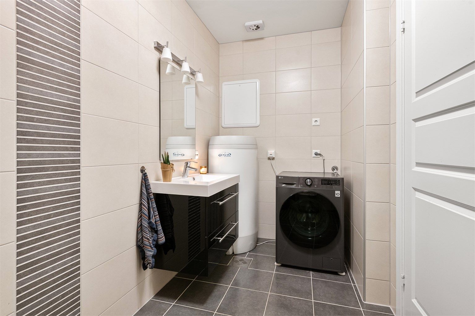 Sort servantinnrending med skuffer og glatte fronter i høyglans. Ovenpåliggende servant med ett-greps armatur. Speil med overlys. Opplegg for vaskemaskin.  Varmtvannsbereder plassert i hjørne