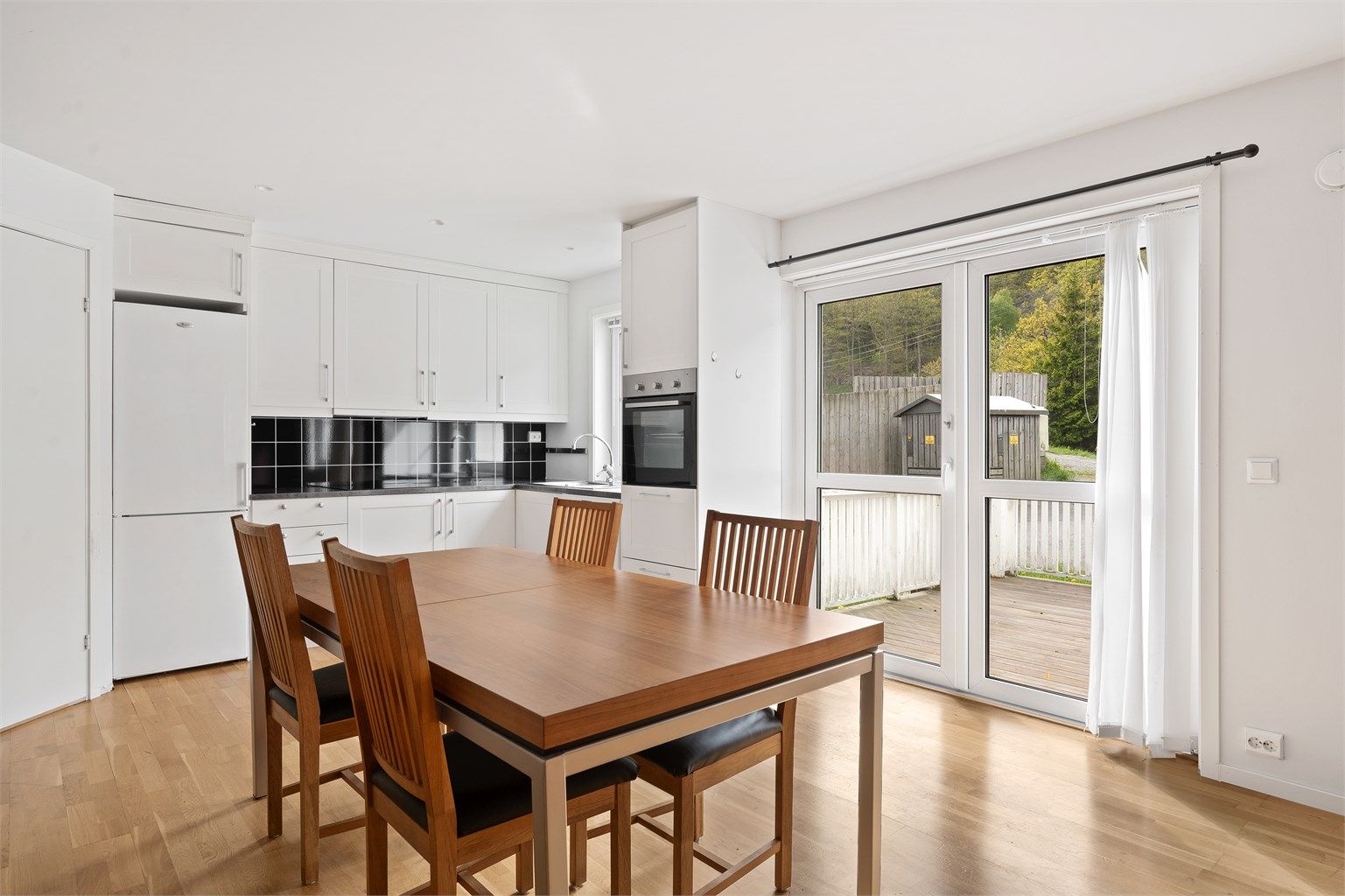 Kjøkkeninnredning med takhøye skap og hvitevarer som medfølger. Store vindusflater som gir mye naturlig lys.