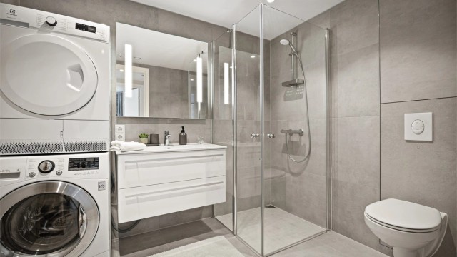 Badet har dusjhjørne med foldedører av glass og opplegg for vaskemaskin/tørketrommel.