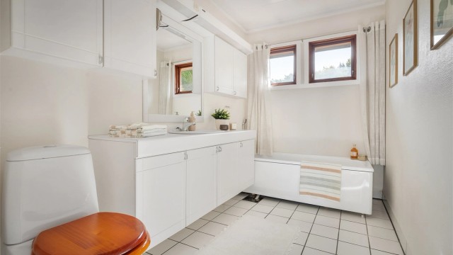 Baderom med gulvstående toalett og badekar med veggmontert hånddusj.